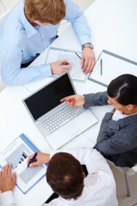 Vue du dessus d'une séance d'évaluation : quatre personnes autour d'une table avec ordinateur et documents